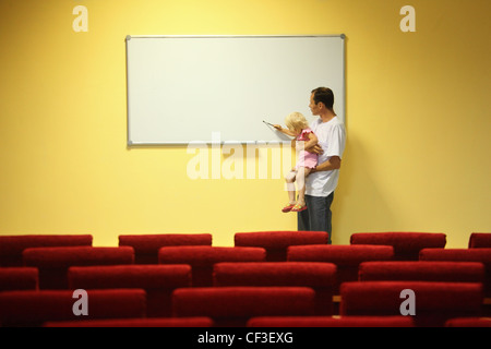 father and little girl in empty presentation hall. little girl is drawing on a board Stock Photo