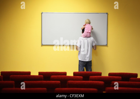 little girl is sitting on father's neck and drawing on a board. chair in out of focus. Stock Photo