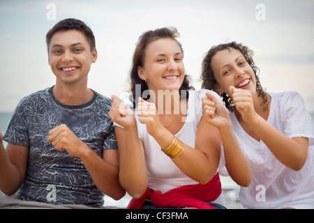 Smiling man and two young women dancing sitting on beach Stock Photo