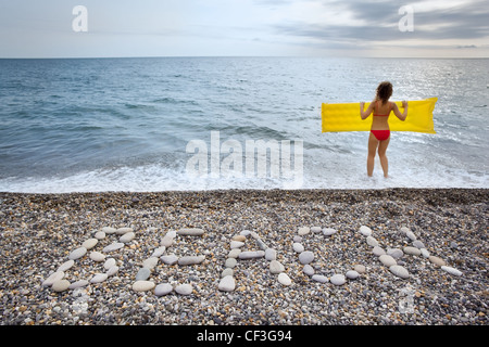 Inscription from stones BEACH at stony coast, young woman keeps in two hands an inflatable mattress on seacoast Stock Photo