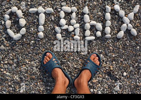 Word rest in Russian combined from white stones on dark pebble, near to feet in slippers.