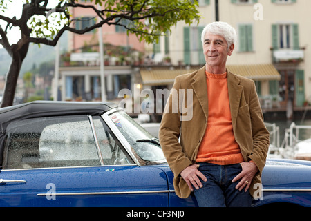 Senior man leaning against vintage car at harbor, Italy, Linfano Stock Photo