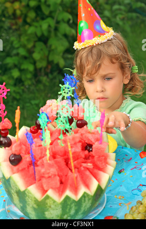 little girl in cap eats fruit in garden, happy birthday Stock Photo