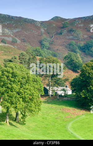 A traditional white washed house situated around Loughrigg Tarn with a dry stone wall separating the fields beyond. Stock Photo
