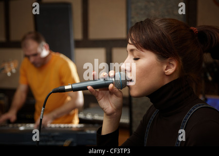 vocalist girl is singing in studio. keyboard player in out of focus Stock Photo