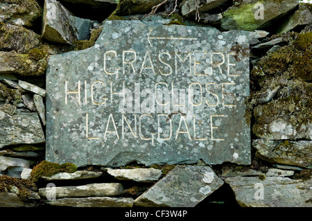 Slate sign showing direction of Grasmere, High Close and Langdale, set in dry stone wall near Loughrigg Fell. Stock Photo