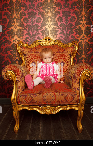 Sad little girl sitting in old armchair. Interior in retro style. Vertical format. Stock Photo