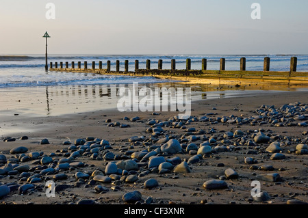 Waves rolling onto the beach past a breakwater. Stock Photo
