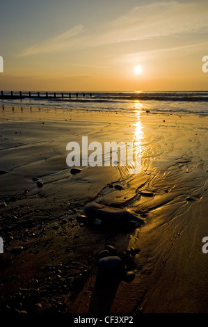 Tide rolling onto the beach past a breakwater at dusk. Stock Photo