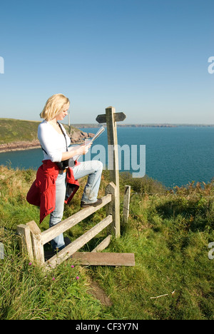 A female walker stops on a stile to read a map on the cliff above At Ann's Head in Wales. Stock Photo