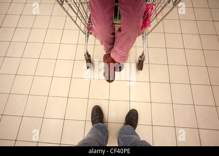 Top view on feet of little girl sitting in shoppingcart and her father standing opposite Stock Photo