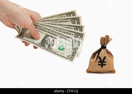 Five 1 U.S. Dollar bills are held in the hand, near by is a money bag with Japanese Yen currency sign, background white. Stock Photo