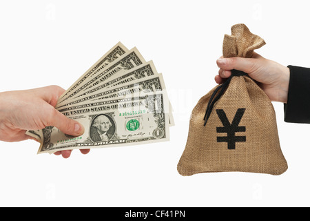 Five 1 U.S. Dollar bills are held in the hand. At the other side a is a money bag with a Japanese yen currency sign. Stock Photo