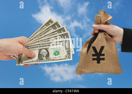 Five 1 U.S. Dollar bills are held in the hand. At the other side a is a money bag with a Japanese yen currency sign. Stock Photo
