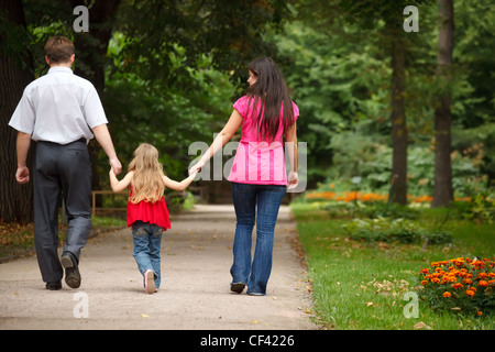 Parents together with daughter walk on summer garden. Leave afar keeping for hands. Stock Photo