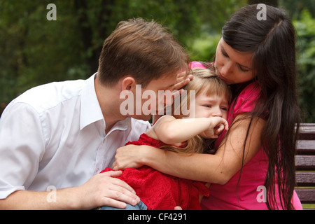 Parents calm crying girl on walk in summer garden. Mum embraces daughter. Close up. Stock Photo