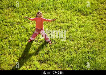 little girl is standing having stretched hands water drain hatch grass field long shadow grass ground field girl looks upwards Stock Photo