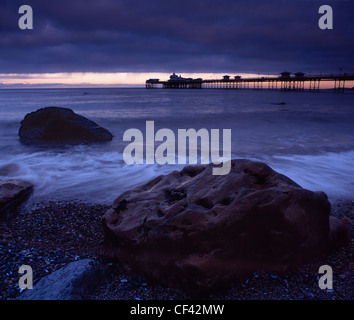 View over large boulders on the seashore towards Llandudno Pier at dusk. Stock Photo