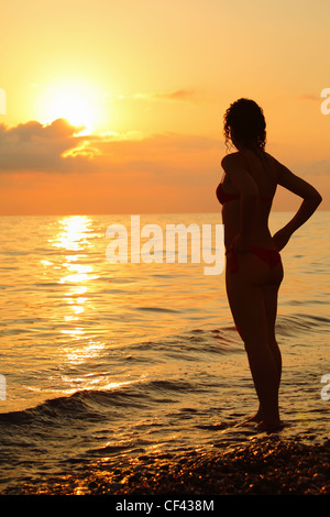 Silhouette beautiful woman standing on beach on sunset Stock Photo