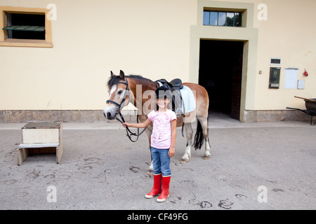 Little girl standing next to her horse ready for a horseback riding lesson.
