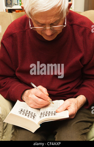 A senior elderly man in his 80's doing a crossword puzzle at home in England , Britain , Uk Stock Photo
