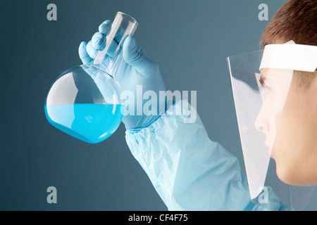 Young scientist looking at blue substance poured in a flask Stock Photo