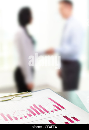 Close up of business graphs with blurred figures of office workers in the background Stock Photo