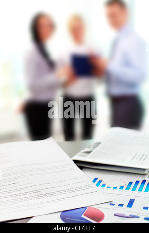 Close up of business graphs with blurred figures of office workers in the background Stock Photo