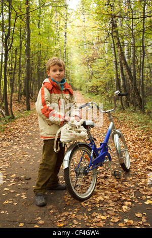 Boy standing next to a bicycle in the autumn park on the road strewn with yellow leaves. Stock Photo