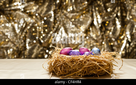 Chocolate Easter eggs in a natural straw nest in front of a beautiful golden background Stock Photo