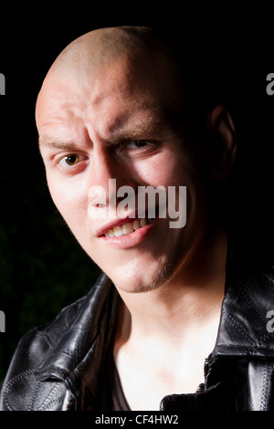 Bald thug in black leather jacket in the dark Stock Photo