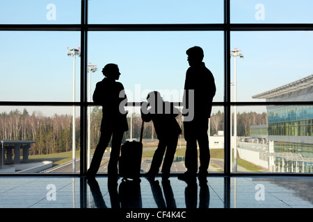 silhouette of mother, father and son with luggage standing near window in airport Stock Photo