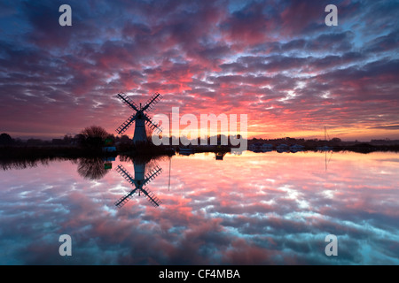 Thurne dyke drainage mill reflected in the River Thurne at sunrise on the Norfolk Broads. Stock Photo
