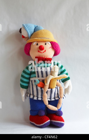 knitted doll, knitted toy with icecream cornet on head and carrot, banana and string of sausages in apron pocket isolated on white background Stock Photo