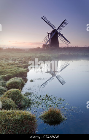 Herringfleet mill or Walker's Mill, a 19th century fully restored octagonal drainage mill reflected in the Broads on a misty aut Stock Photo