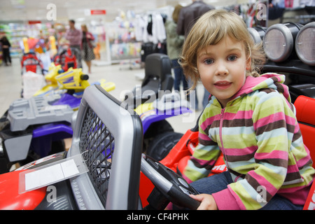little girl in supermarket alone, chooses in department of toys. sits in an electromobile Stock Photo