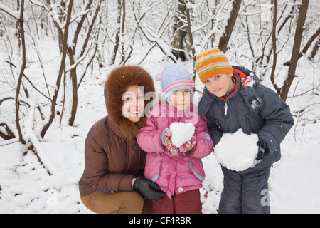 young woman with boy and little girl in winter in wood, children keeps in hands snowballs Stock Photo