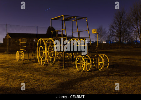 A childrens climbing frame in the shape of a tractor in a playground area at night.