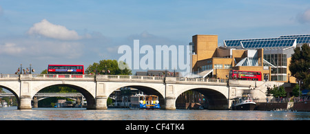 Red double decker buses crossing Kingston Bridge over the River Thames as a pleasure boat passes below. Stock Photo