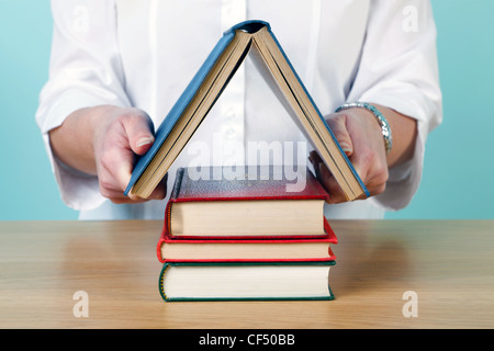 Photo of a woman making a house shape from old hardback books. Stock Photo