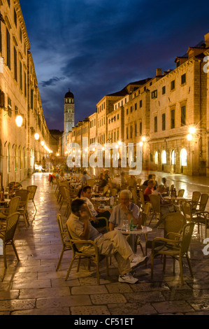 People eating at restaurants main street with Franciscan Monastery tower at dusk, Old City of Dubrovnik, Dubrovnik, Croatia Stock Photo
