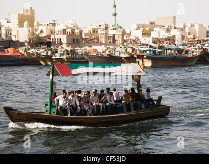 UAE, Gulf State, Dubai, Abra water taxis passing on the Creek with skyline and souk market on the far shore by moored dhows. Stock Photo
