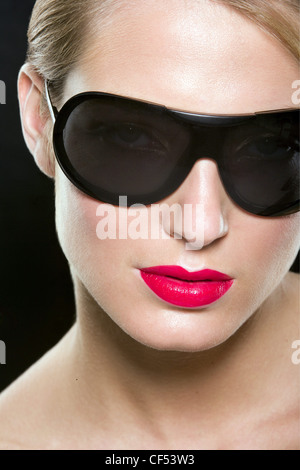 Female with blonde hair wearing worn tied up wearing bright red lipstick and large black sunglasses Stock Photo