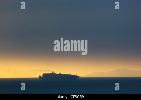 Tarifa, Cadiz Province, Spain. Cargo ship passing through Straits of Gibraltar at dawn. Coastline of Morocco in background. Stock Photo