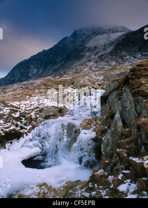 Small waterfall and partly frozen pool on a stream flowing down from Llyn Bochlwyd to Llyn Ogwen. The dark mass of Tryfan is bey Stock Photo