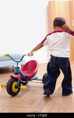 Male toddler with brunette, wearing red and white t shirt and jeans, pulling a tricycle at home Ian Boddy Stock Photo