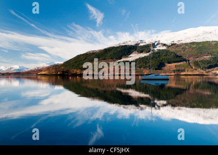 A boat and snow capped mountains reflected in Loch Leven Glencoe. Stock Photo