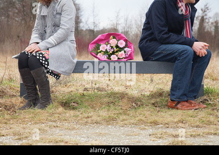Couple with difficulties sitting on bench with bouquet in between Stock Photo