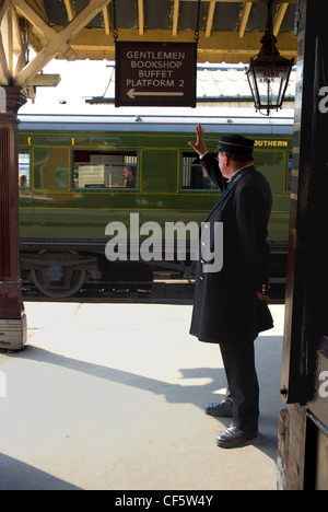 The Station Master waves a train off at Sheffield Park Station on the Bluebell Railway. Stock Photo