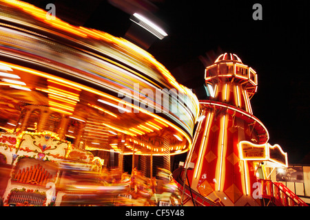 Light trails from a carousel as it whizzes round in a fairground at night. Stock Photo
